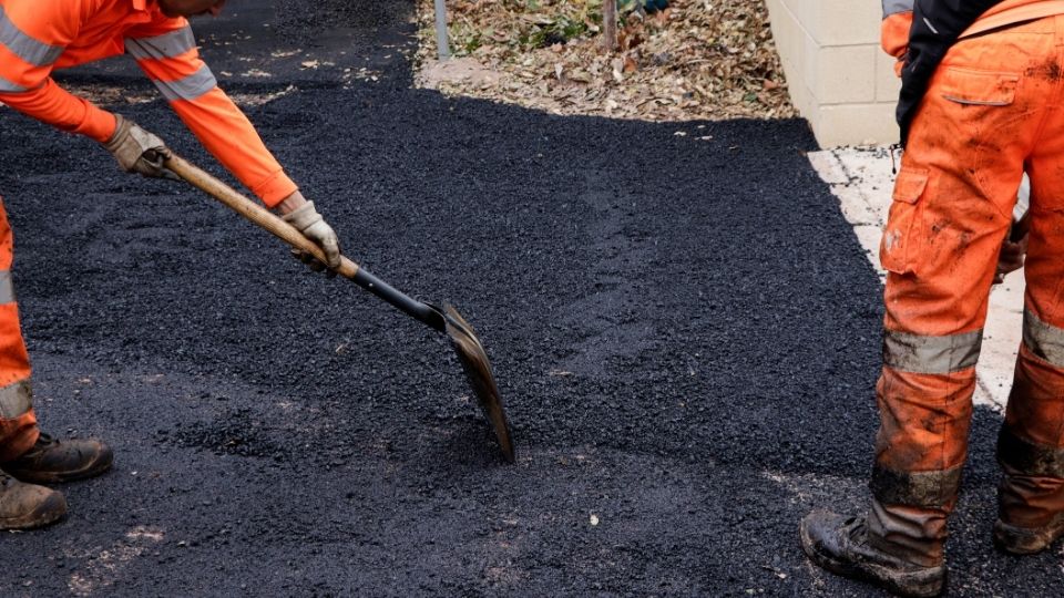 Crew repairing a commercial asphalt driveway with fresh hot mix asphalt